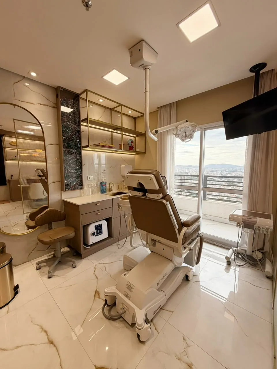 Sala de atendimento da Clínica ORA com cadeira odontológica, foco cirúrgico e janela com vista da cidade